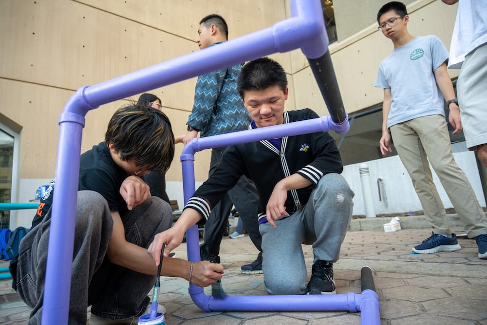 Students collaborate on painting a large pipe installation.
