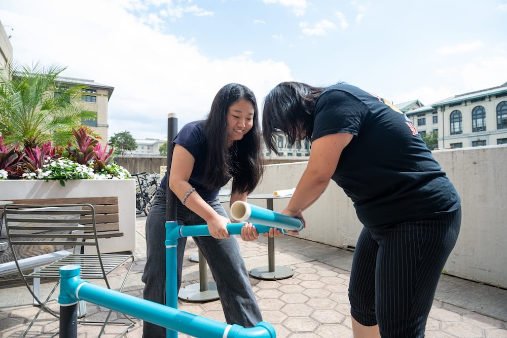 Students collaborate on painting and assembling a large pipe structure.