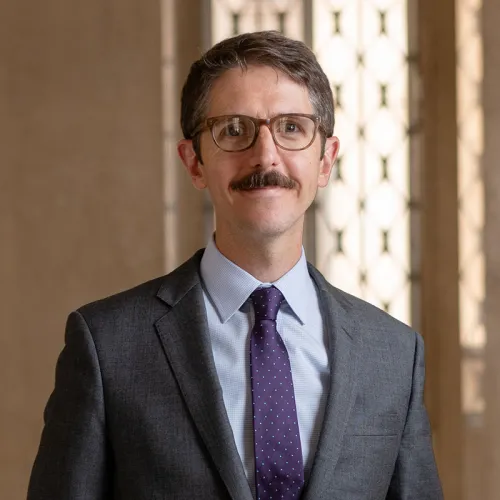 Daniel Kasper - white male with glasses and mustache wearing a gray suit and tie