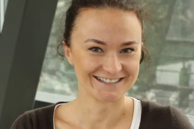 Anna Kietrys - smiling woman in a brown sweater and white shirt with dark haired pulled back