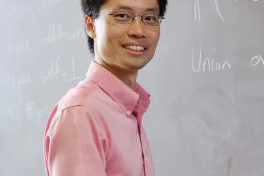 Po-Shen Loh - asian male at chalkboard smiling at camera