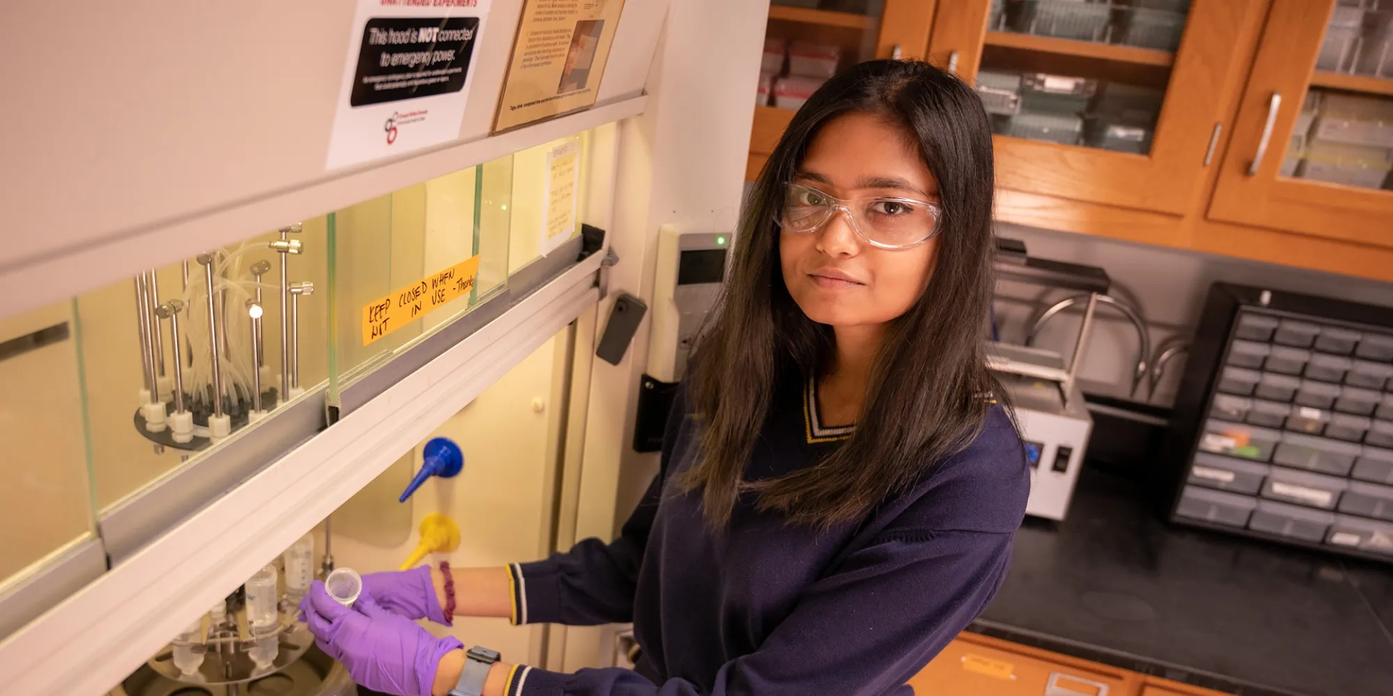 Leenia Mukhopadhyay works under a lab hood as she mixes chemicals