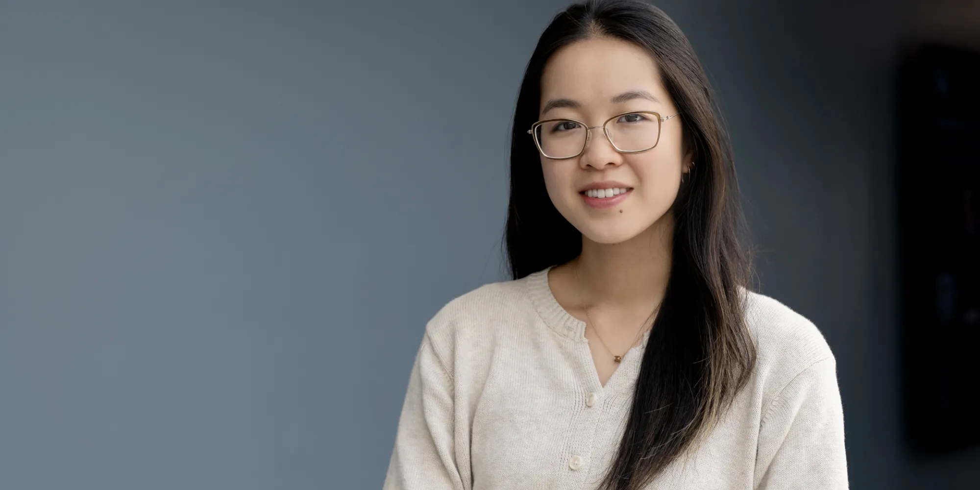 Smiling young woman wearing eyeglasses posing against a neutral background.