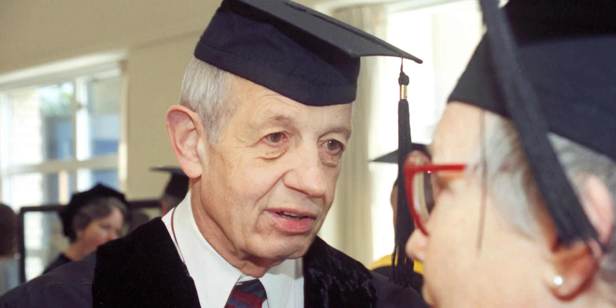 John Nash earns an honorary diploma from Carnegie Mellon University. He stands in graduation regalia and speaks with another person.