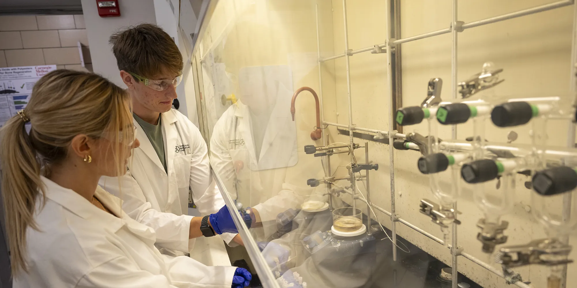 Chloë Zimovets and Luke Cerwin work at a fume hood as they mix chemicals.