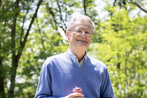 Emile Bominaar stands outside in front of a group of trees. He smiles at the camera.