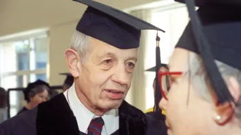 John Nash earns an honorary diploma from Carnegie Mellon University. He stands in graduation regalia and speaks with another person.