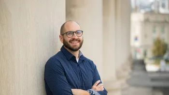Kevin Hunter stands outside of Mellon Institute and leans against one of the pillars. He smiles at the camera.