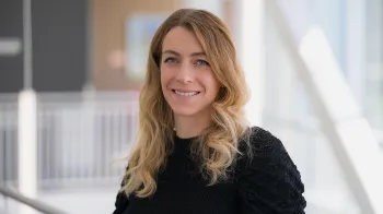 Antonella Palmese stands in a white hallway with large windows. She smiles at the camera.