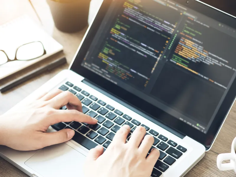 Image of hands on a laptop keyboard with coding on the screen.