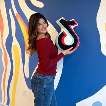 Woman holding the Tik Tok logo in front of a colorful wall