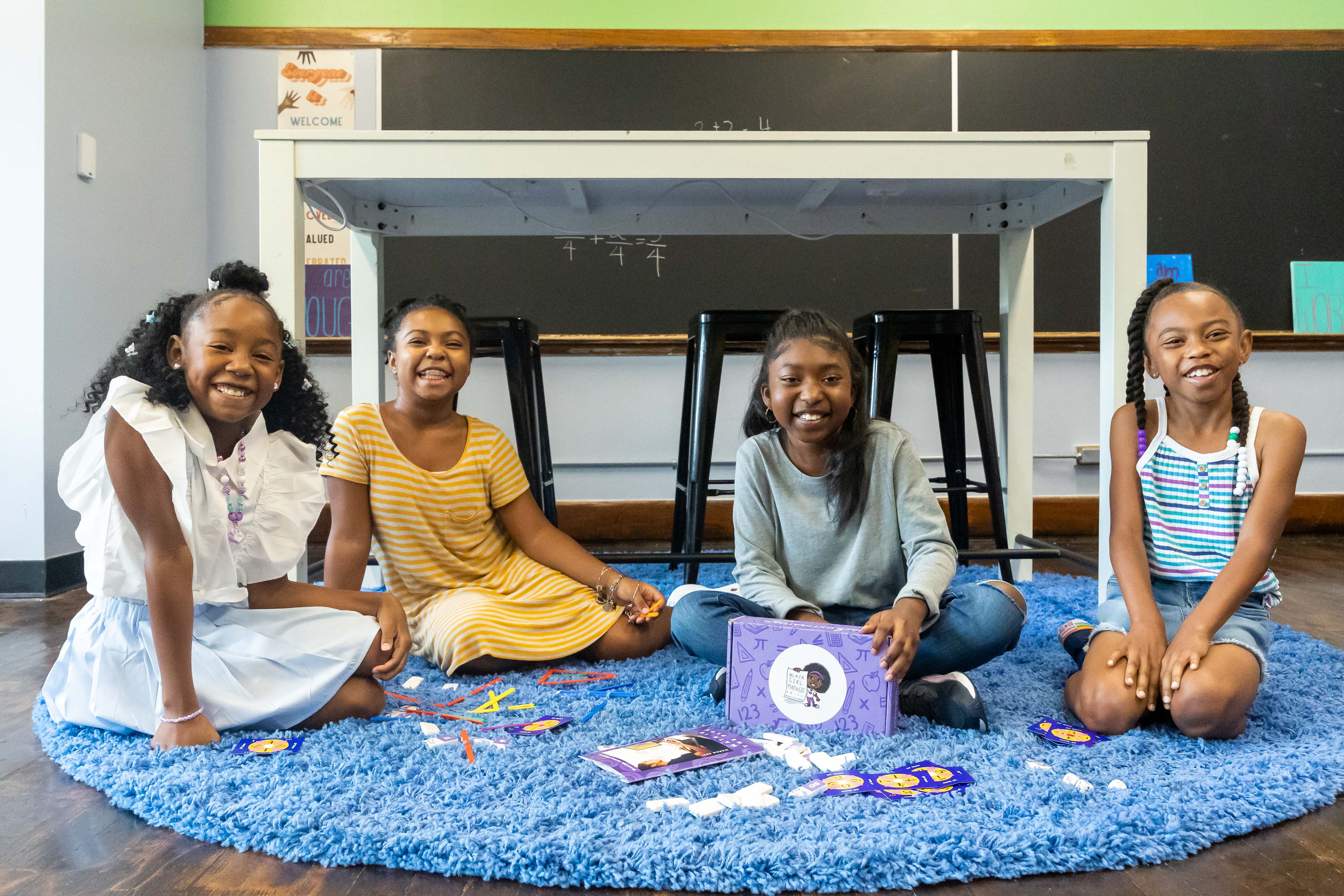 Four girls sit on a carpet with kit boxes