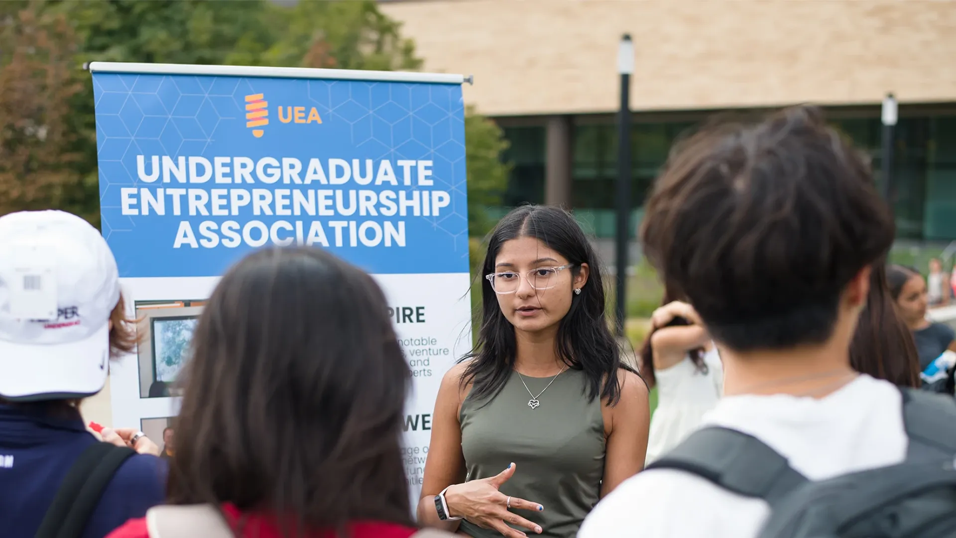 Undergraduate student talking to other students about their club out on the front lawn of the Tepper School quad