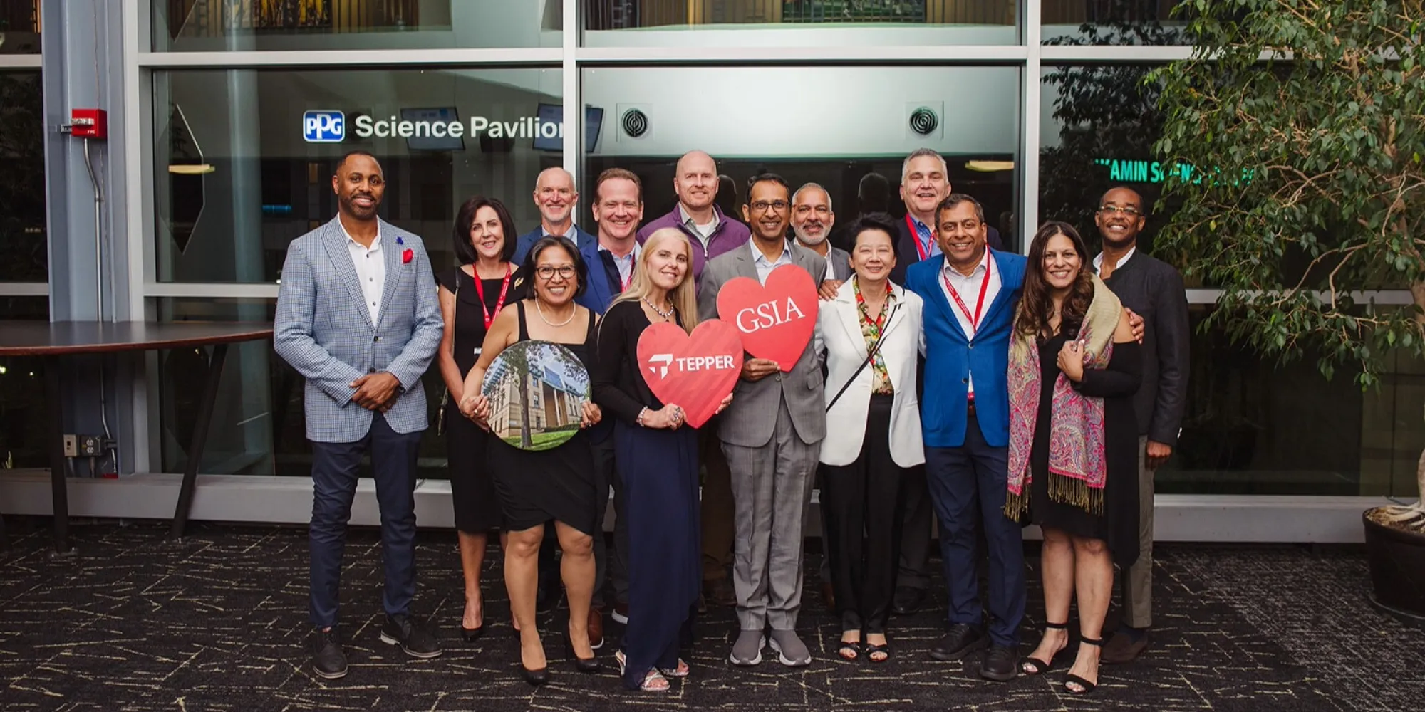 A group photo of several alumni at the Reunion Celebration, holding up Tepper School signage