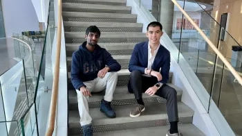 Ethan Hilton and Ayushman Srivastava sit on the stairs in the Tepper School lobby.