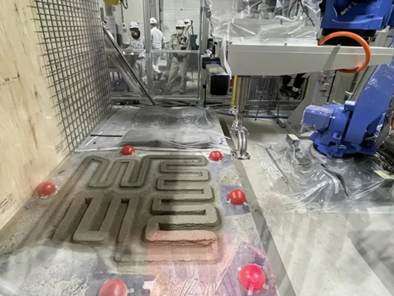 Spray-based concrete 3D printing lab with workers in the background.