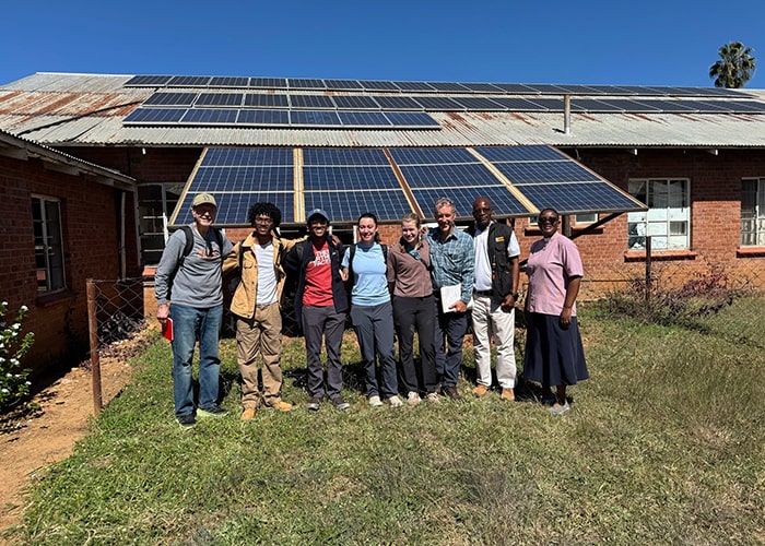 a large group of students in front of a structure with solar panels on the roof