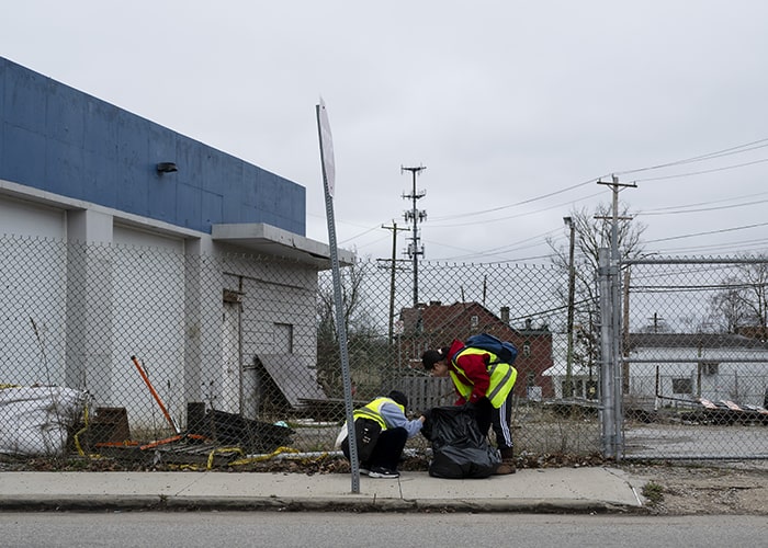 two students pick up trash along a city street on the north side of Pittsburgh