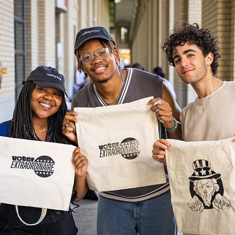 Students hold up their freshly screen-printed tote bags that read, "Voter Extraordinaire," for Democracy Day on CMU's campus.