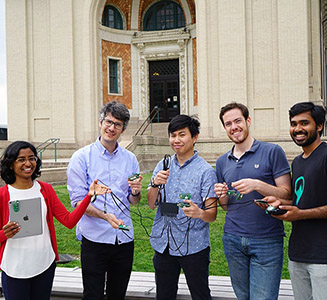 group of students smiling and holding a laptop and wires