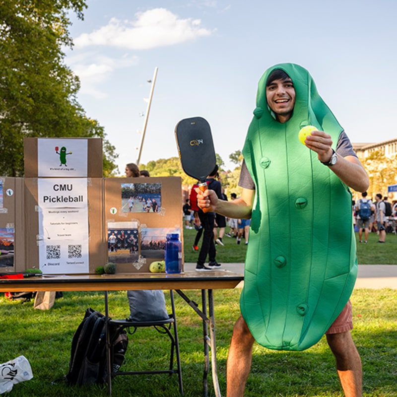 A member of the CMU Pickleball Club dressed in a giant pickle costume invites members to join during The FAIR.