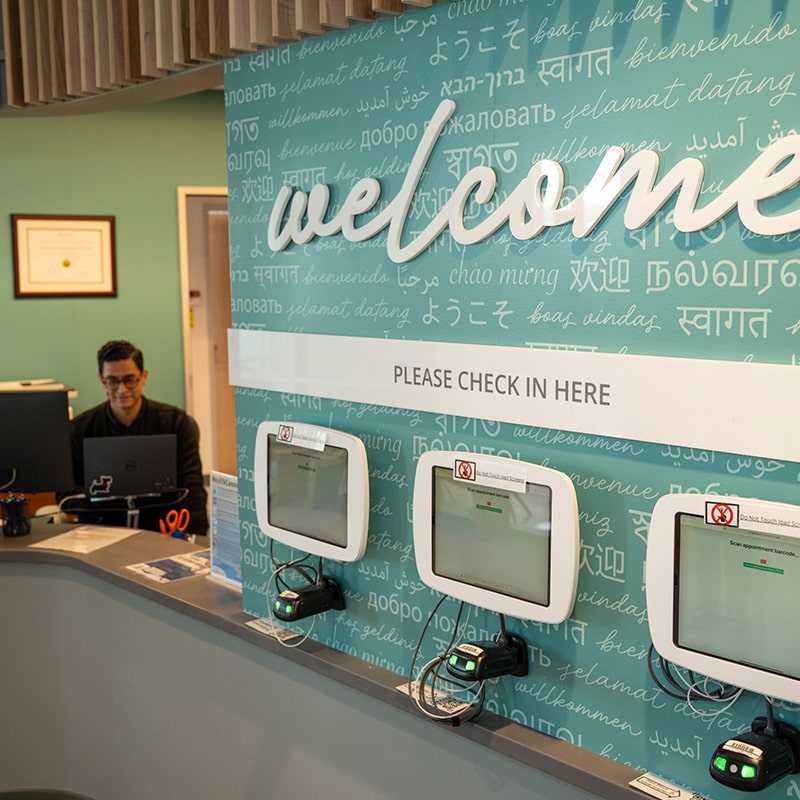 University Health Services receptionist smiles in the reception area, which is also equipped with digital sign-in tablets.