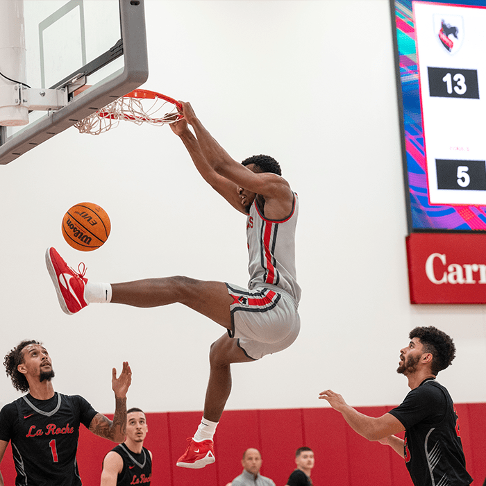 Basketball team player dunks and hangs on the hoop during a game in the Highmark Center for Health, Wellness, & Athletics