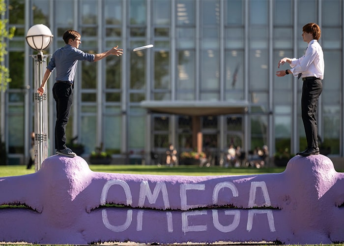 First-year students both with the ultimate frisbee club throw frisbee while standing on The Fence.