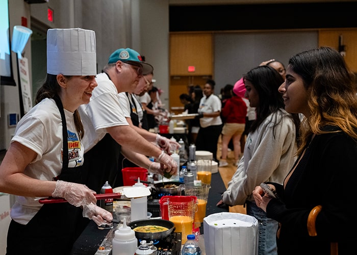 CMU staff and faculty are lined up to serve students breakfast food for Almost Midnight Breakfast