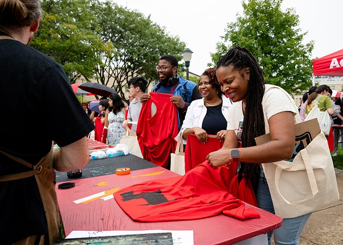 A student and his family tries screenprinting on the East West Walkway for Scotty Saturday
