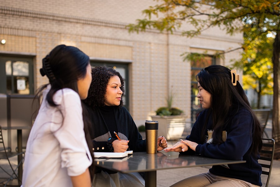 Staff member meets with students at a table in Legacy Plaza