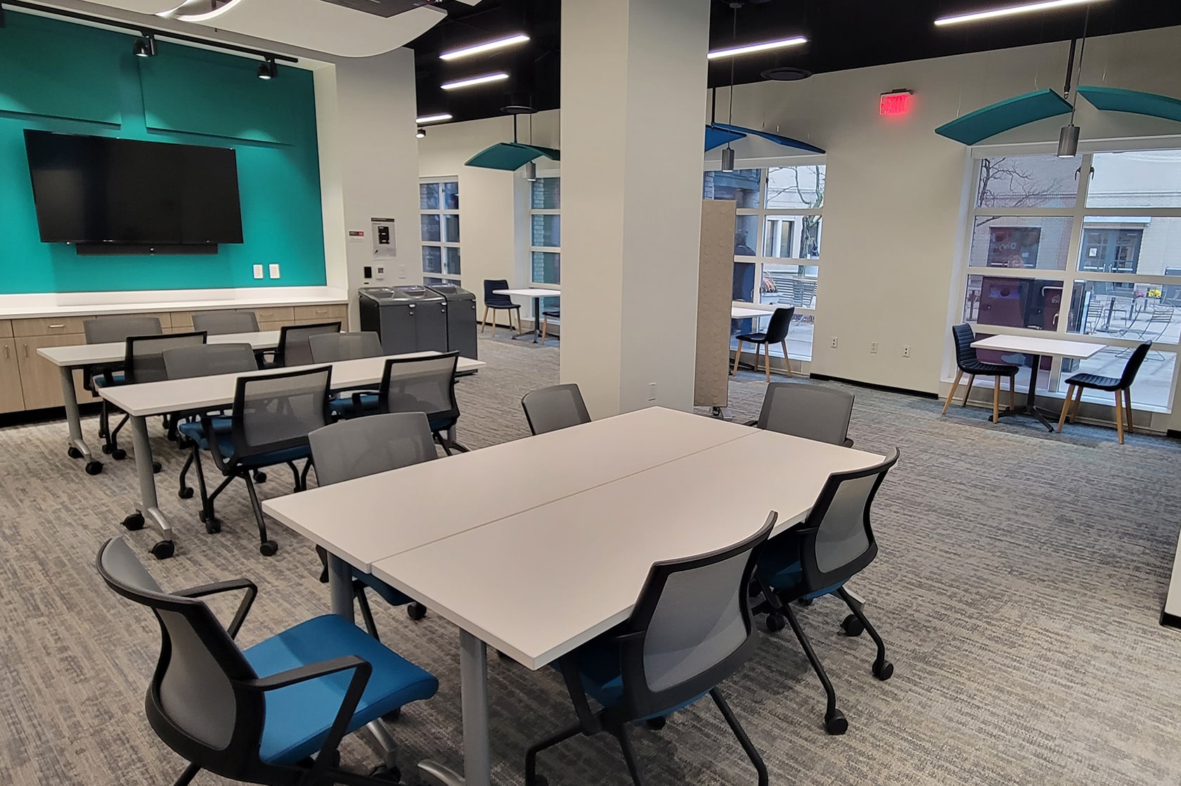 tables and chairs set up facing a teal all with a digital display on it