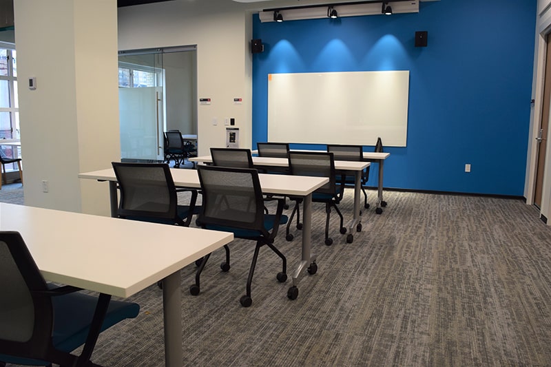 tables and chairs facing a white board and blue wall