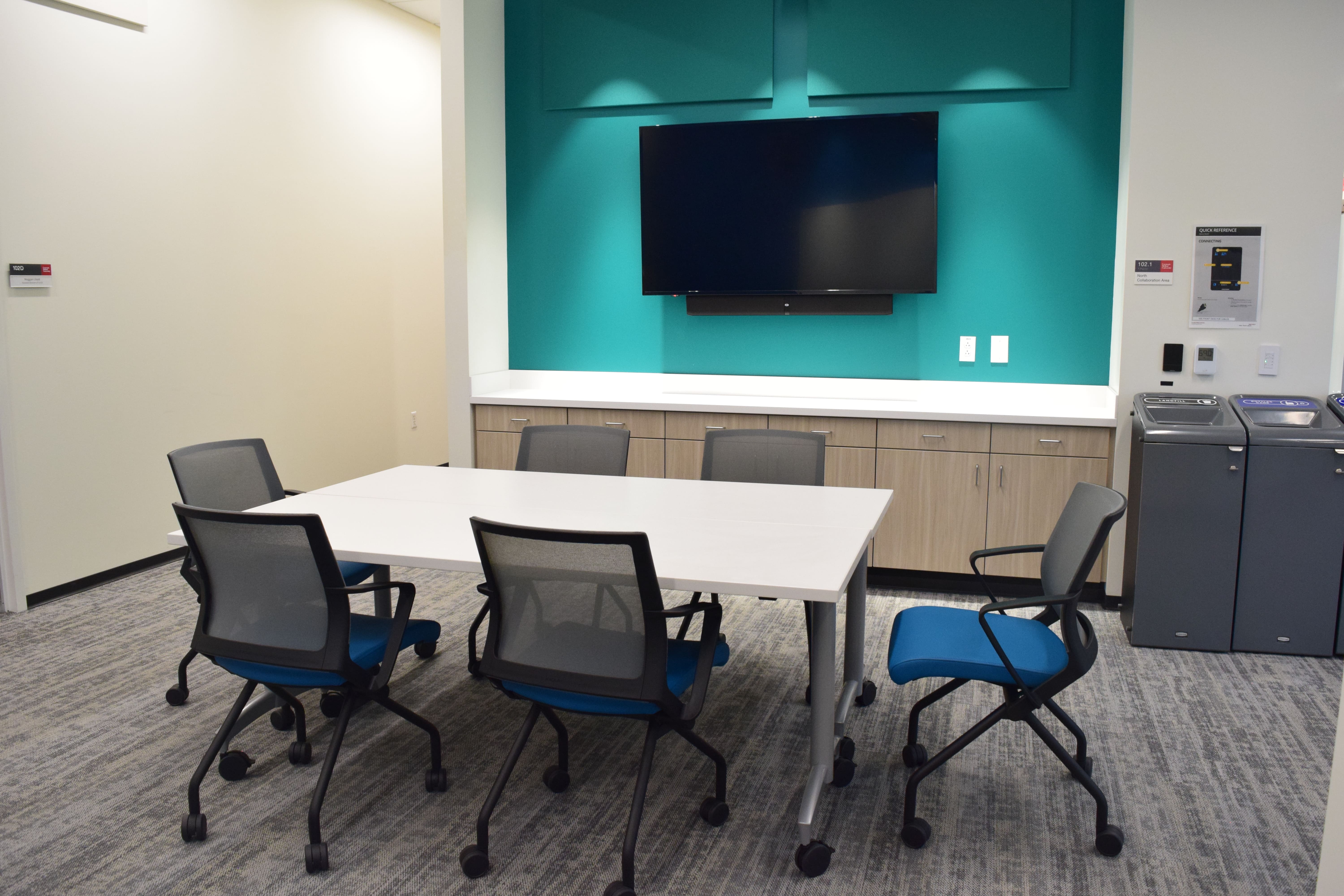 table with chairs in front of large flat panel monitor on green wall