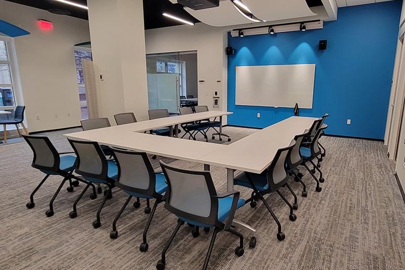 tables and chairs designed in a u shape in front of a white board and blue wall
