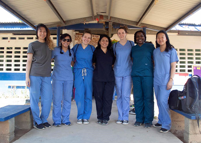 students in medical scrubs smiling and standing in front of a hospital