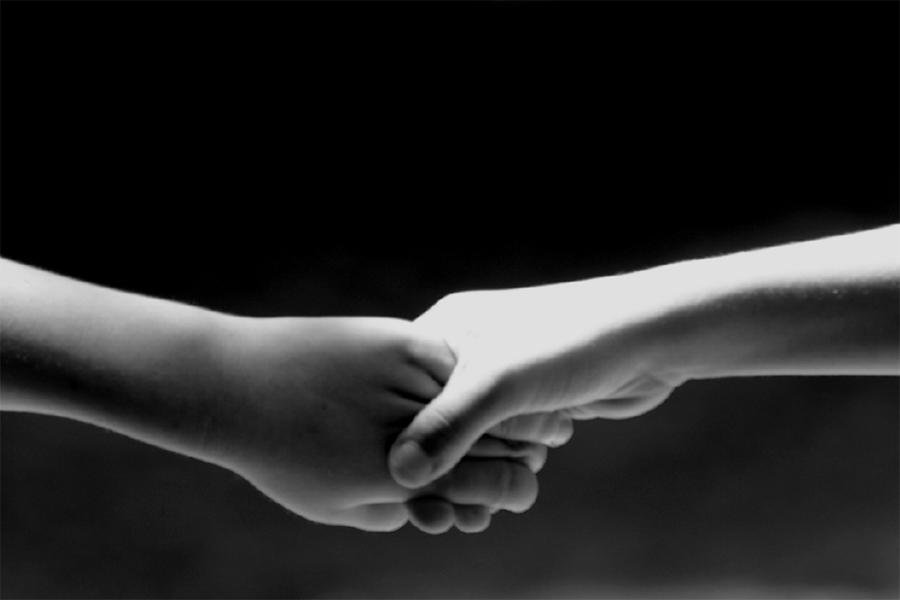 Black and white image of two hands reaching and holding each other against a black backdrop
