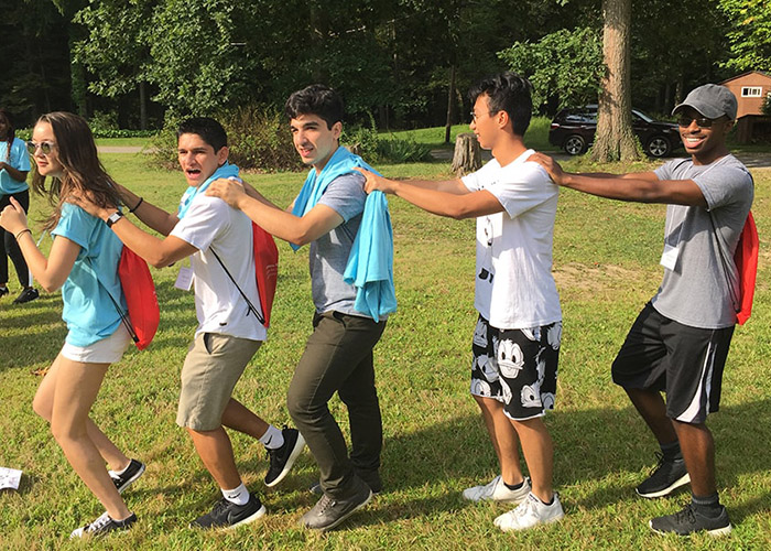 Students at ORIGINS hold each other's shoulders in a single file line during a game