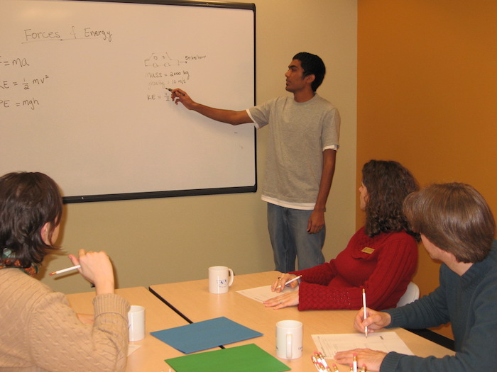 student pointing at dry-erase whiteboard while other student look on