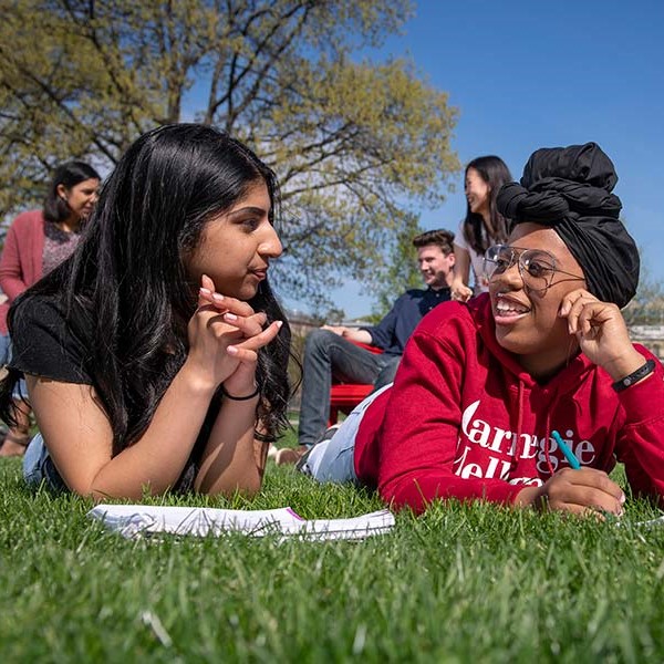 two students laying in the grass with a notebook in front of them