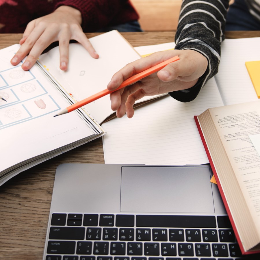 students sitting side by side with laptop and textbooks on table