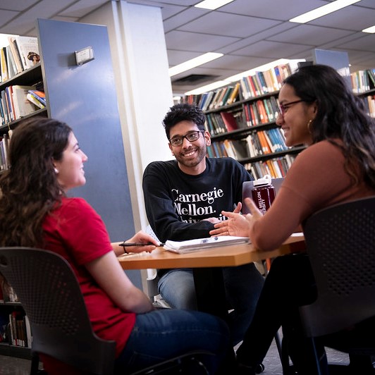 three students sitting around a table in a library