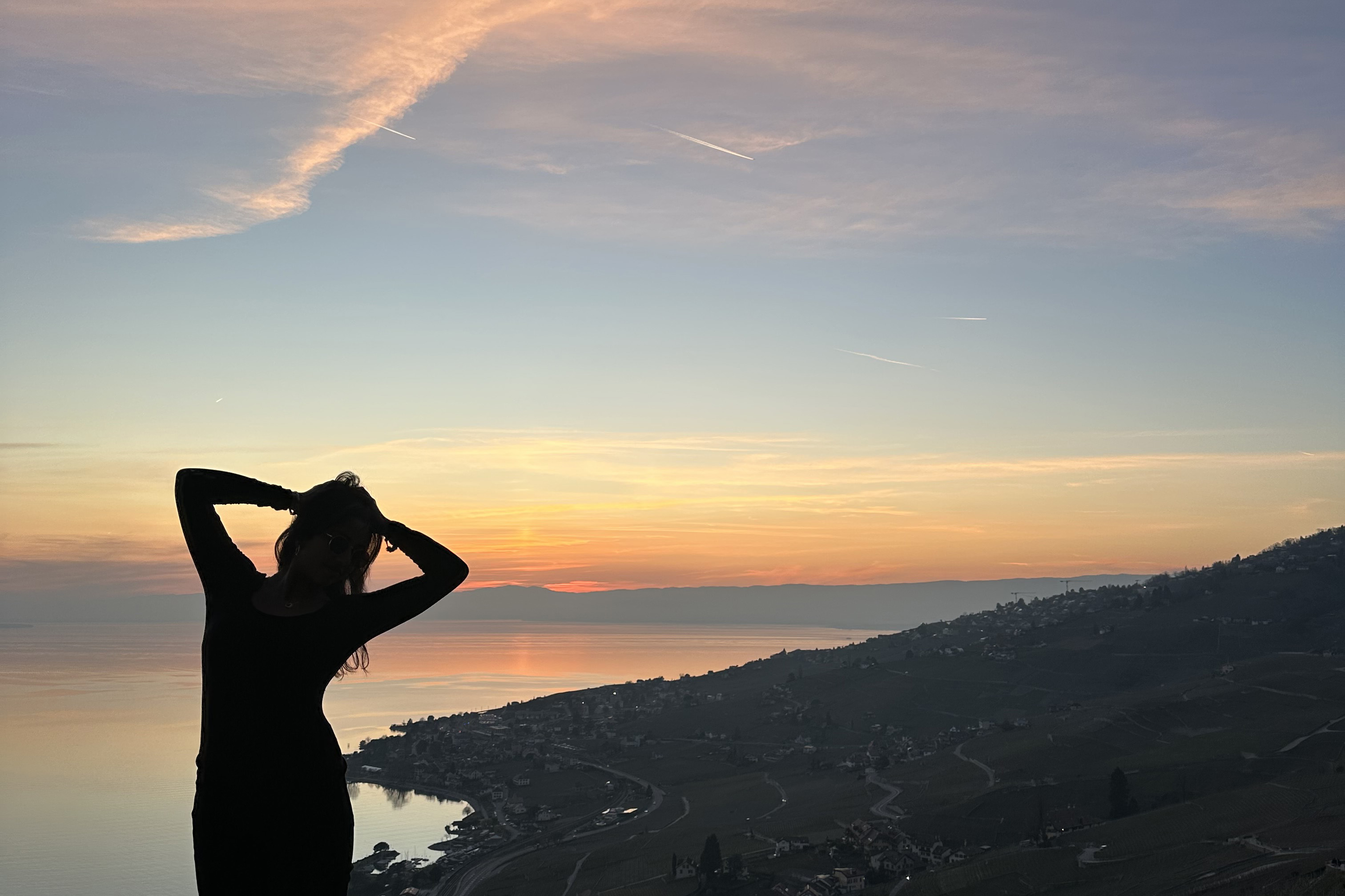 Image of kundhavi's silhouette standing on top of a cliff over looking the water at sunset