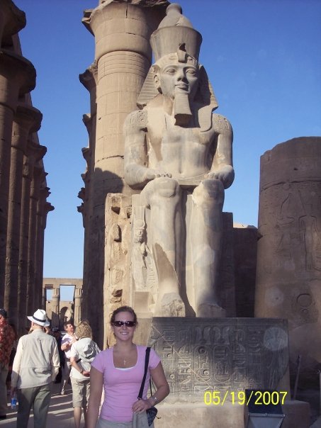 Kensee poses in front of a statue of an Egyptian Pharaoh which towers several stories above her head.