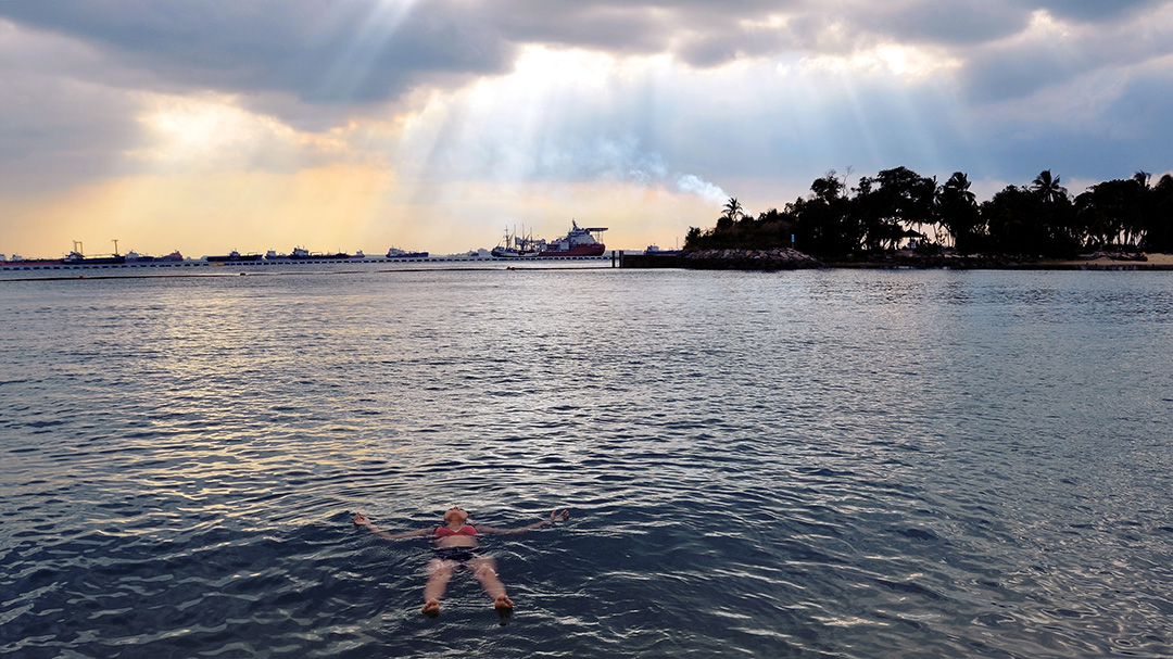 Christina floats on her back in an ocean at sunset.
