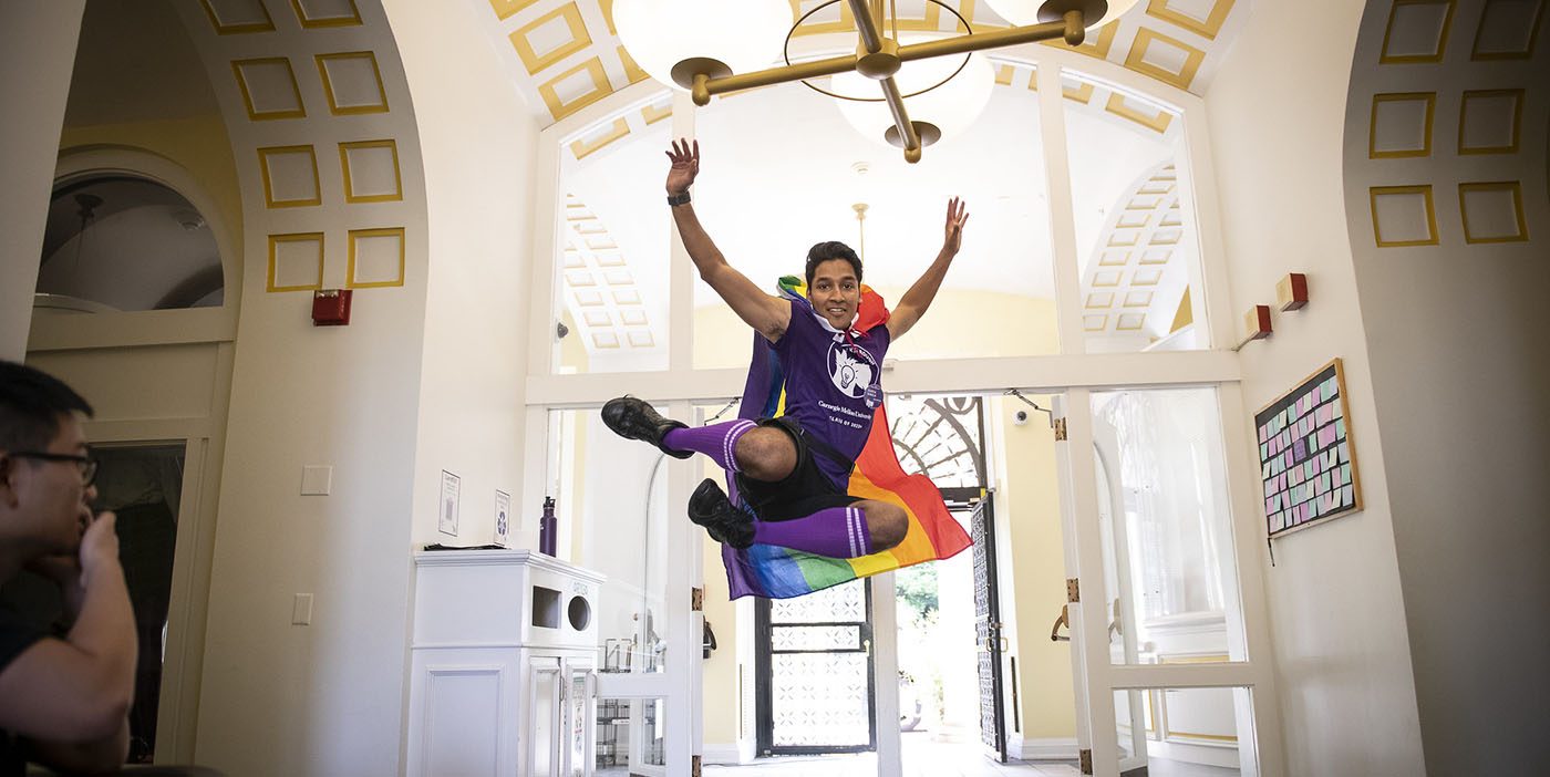 Student in a rainbow cape jumps in the air.