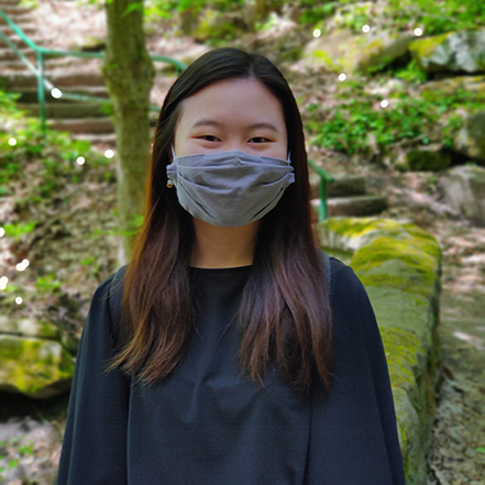 Claire Chiang poses in front of trees, wearing a mask as a COVID precaution.