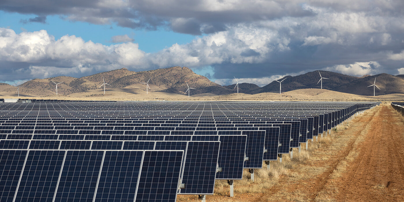 photo of solar panels and windmills against mountain background with blue sky