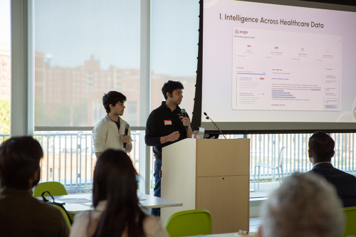 Two men standing in front of a screen presenting to a group