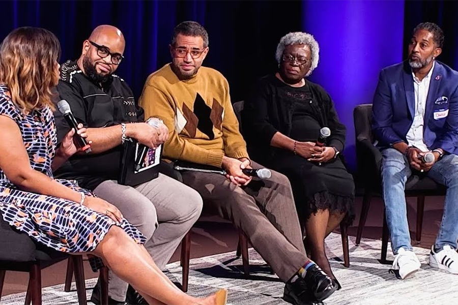 A group of Black professionals sitting on stage participating in a question and answer session. 